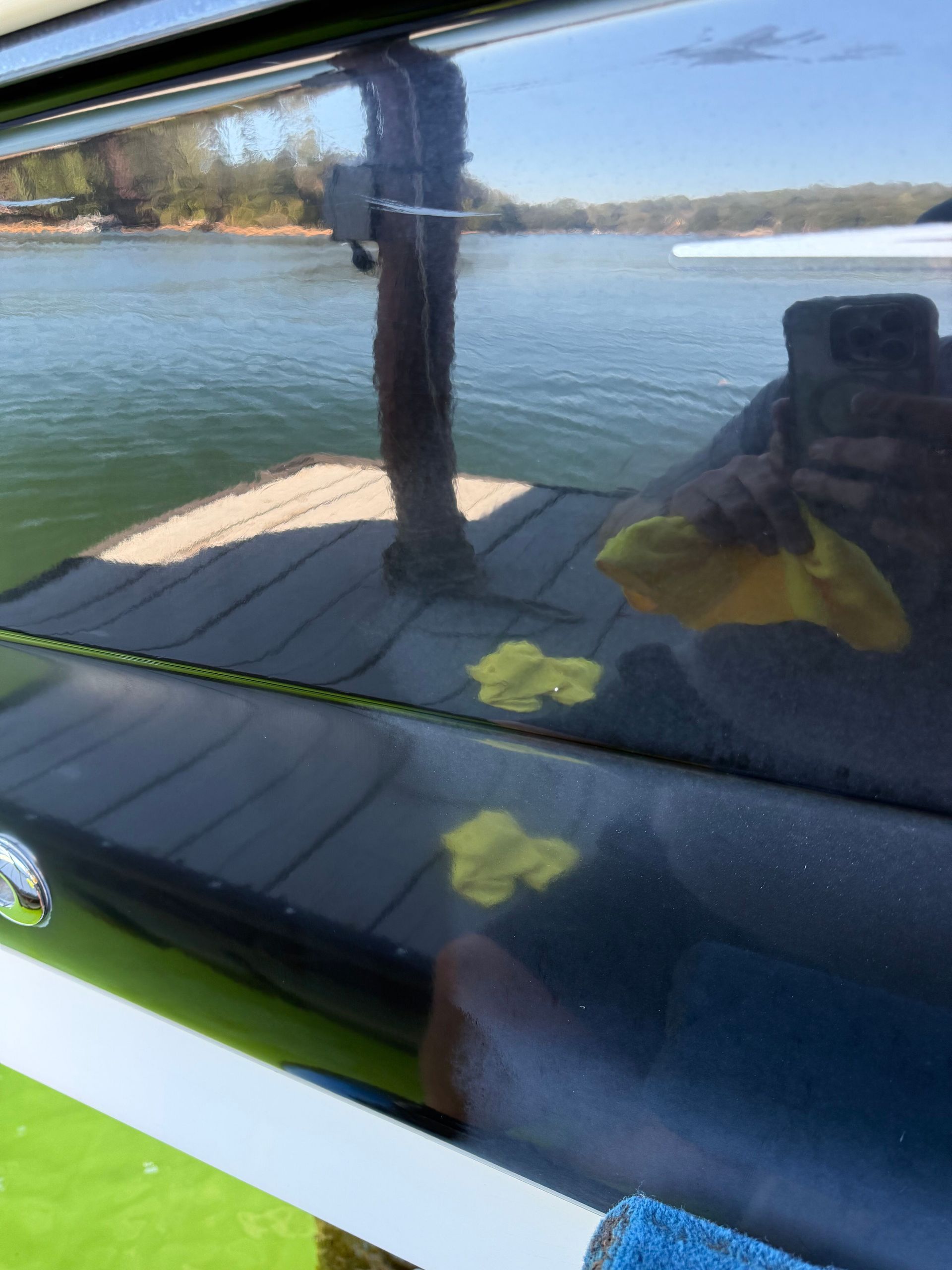 Boat deck reflecting a dock, water, and yellow cleaning cloth.