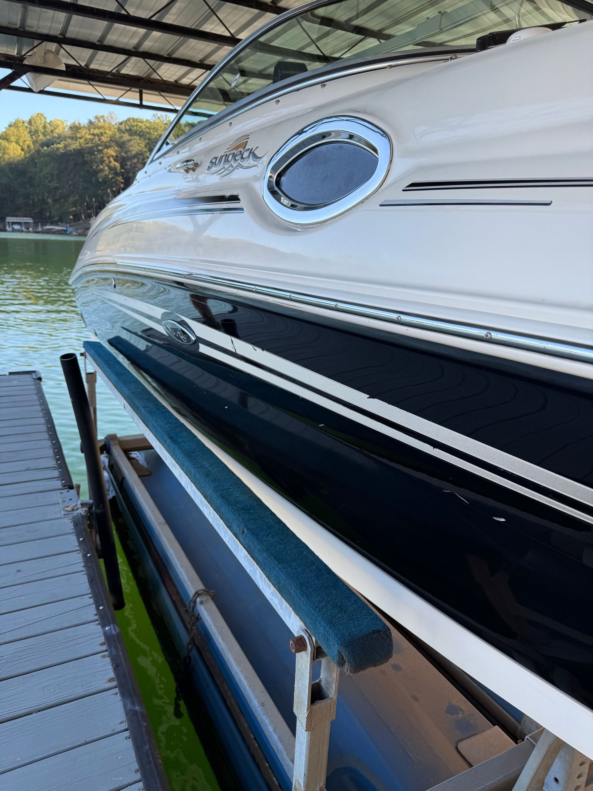White and black boat at a dock on the water, with an oval porthole window and a blue bumper.