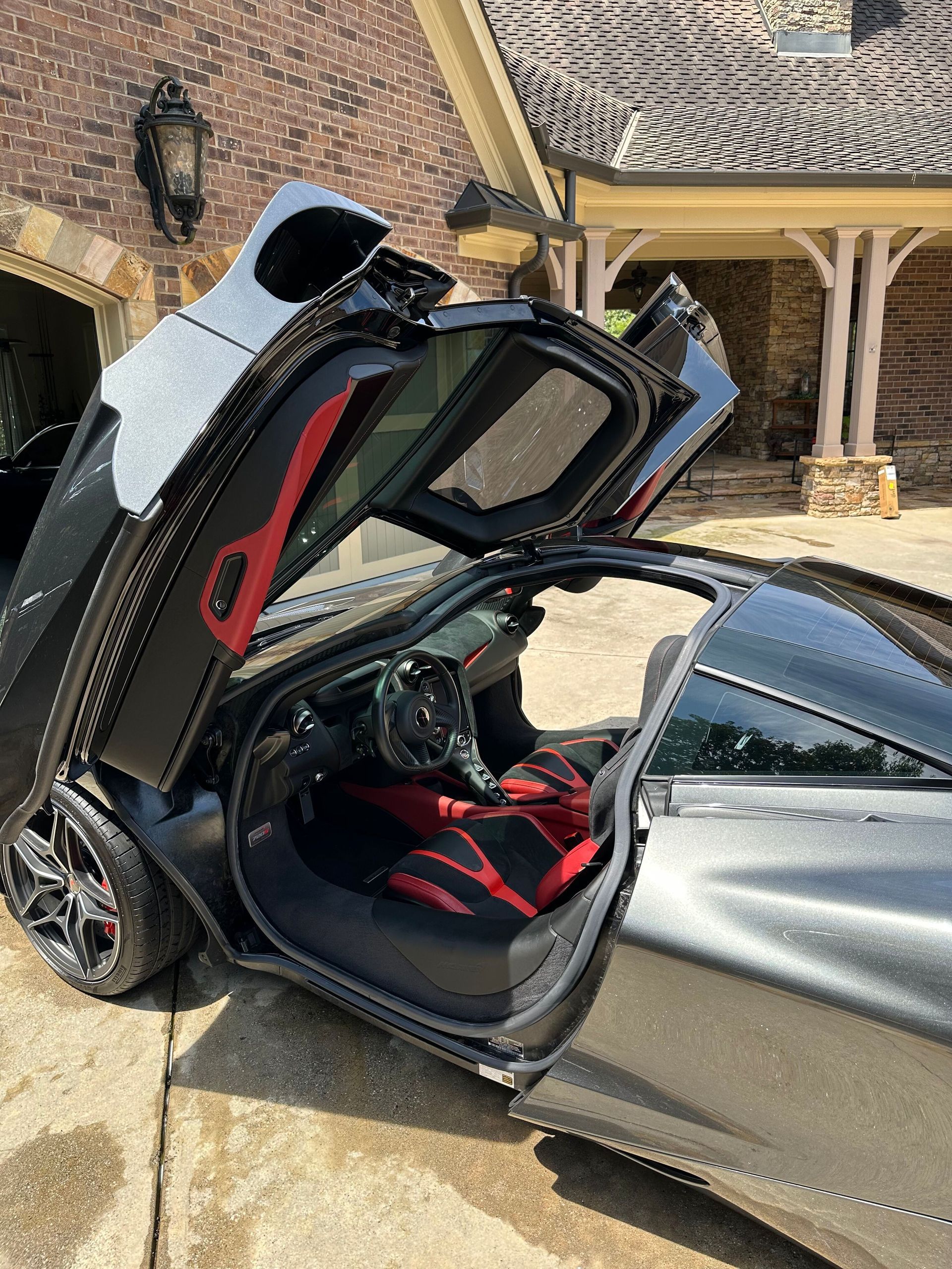 Black sports car with doors open, red interior, parked outside a brick building.