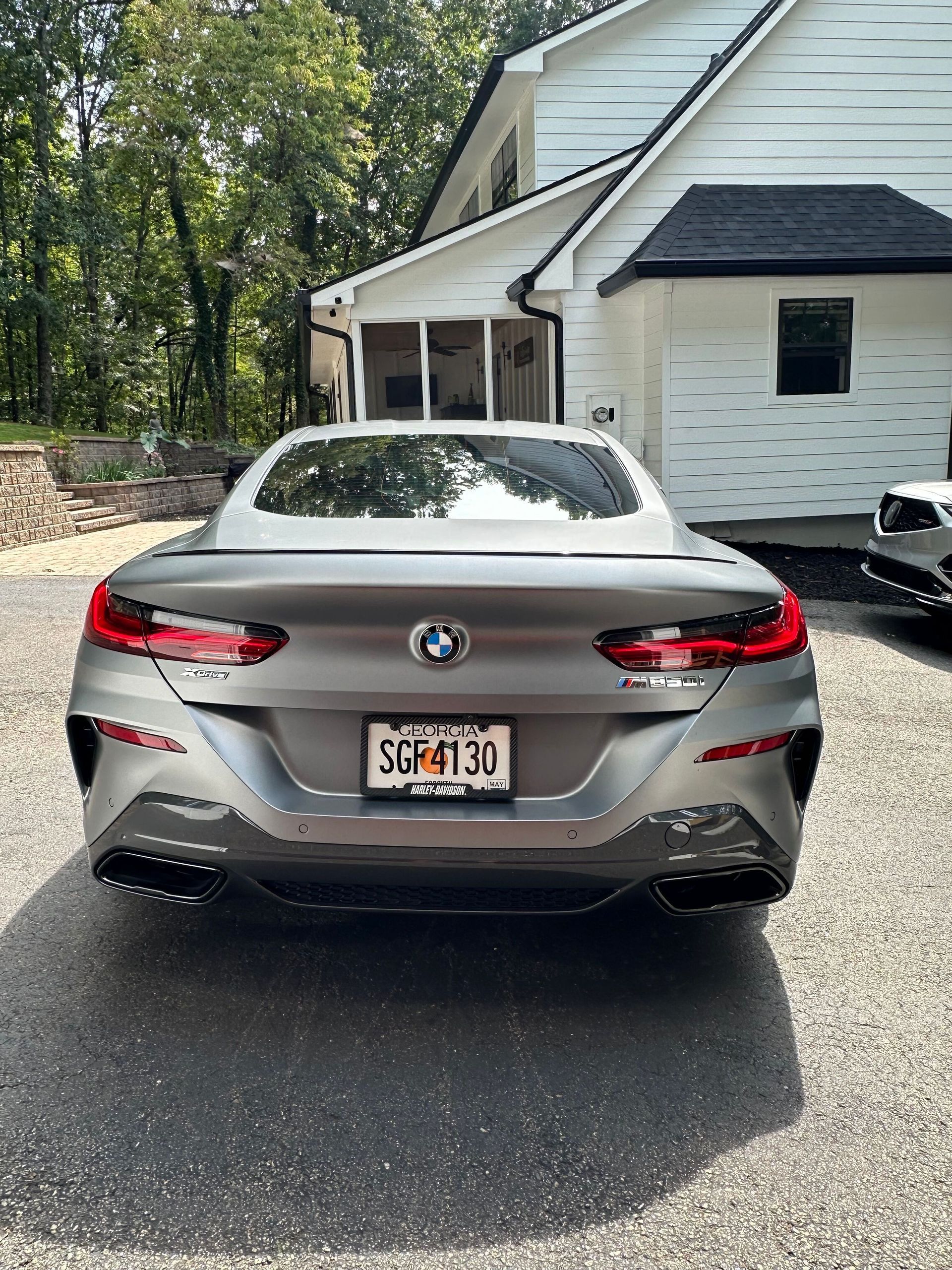 Rear view of a gray BMW 8 Series Gran Coupe parked on a driveway in front of a white house.