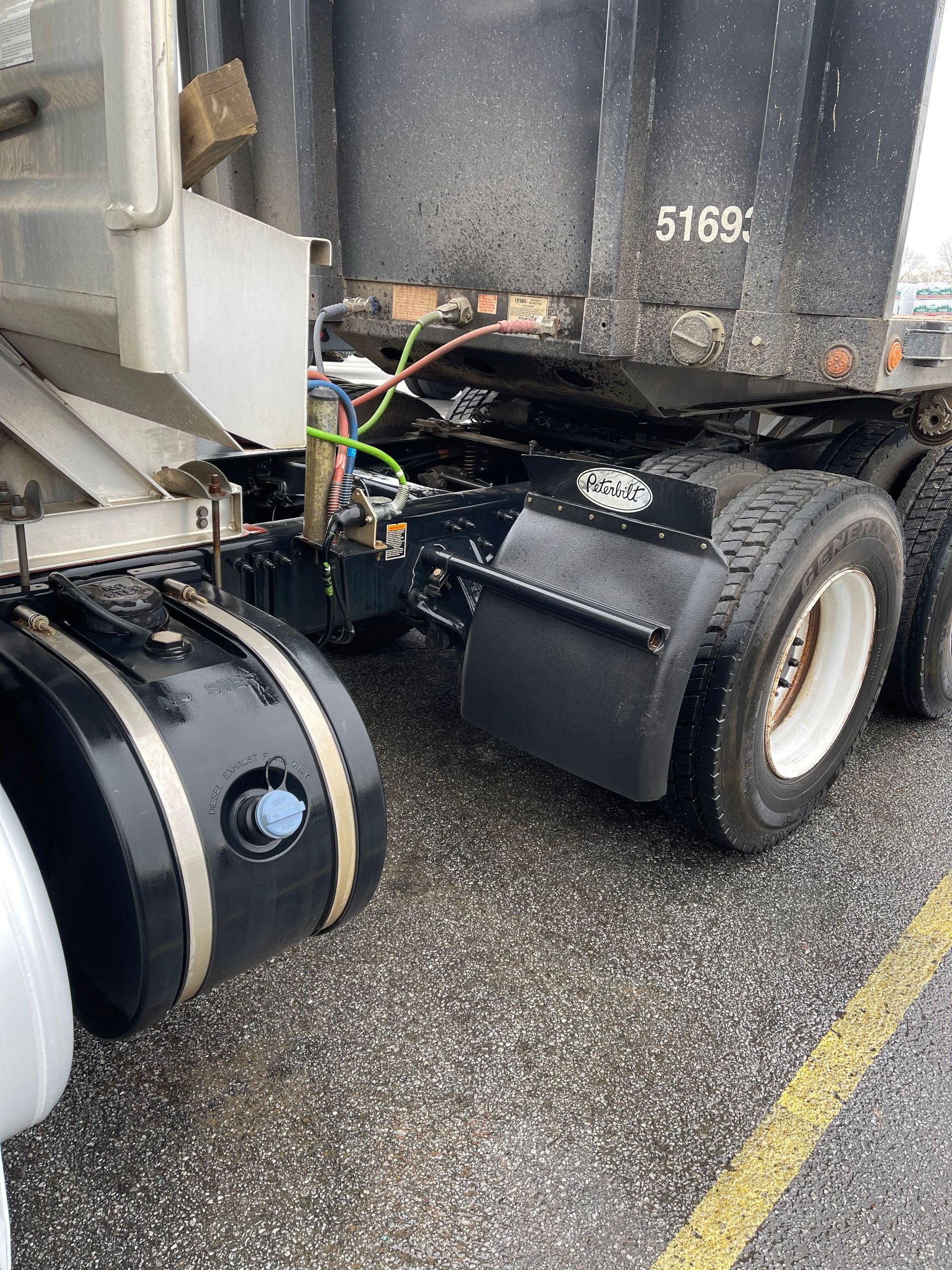 Black semi-truck detail; tires, fuel tank, and mud flaps are visible on the side. Asphalt surface.