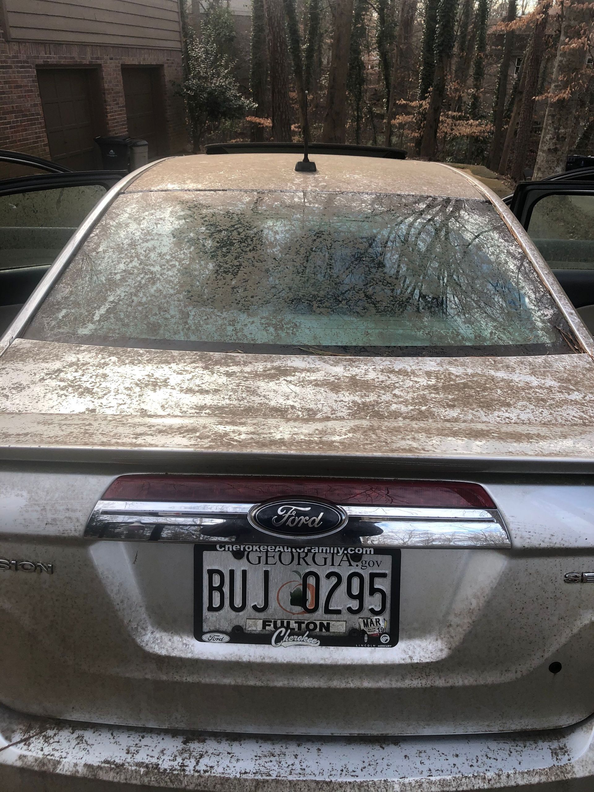 A silver Ford sedan covered in pollen. Georgia license plate, BUJ 0295. Outdoors.