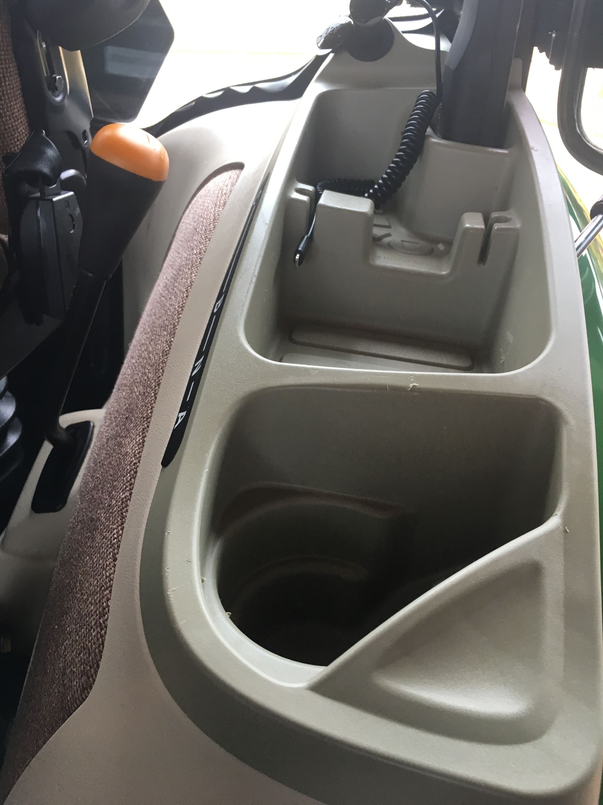 Tan and green tractor console with cup holders and storage compartments.