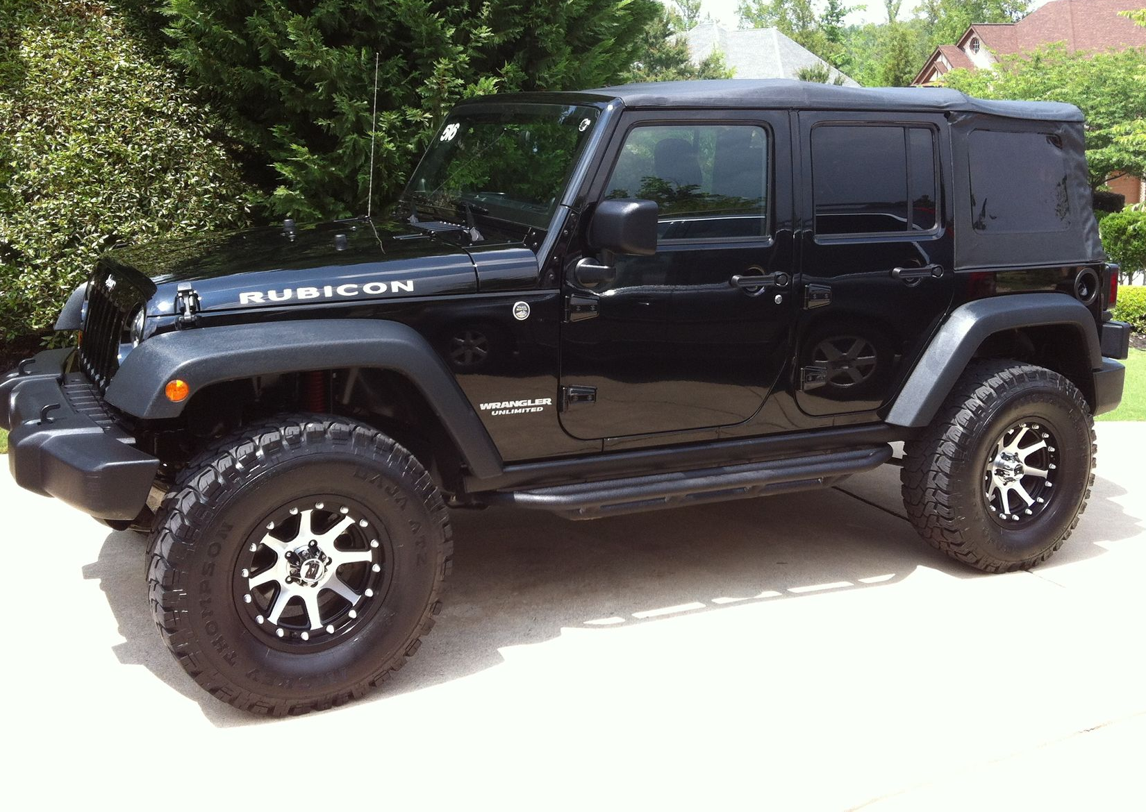 Black Jeep Rubicon parked on a paved driveway; black wheels, dark tinted windows, and a black hardtop.