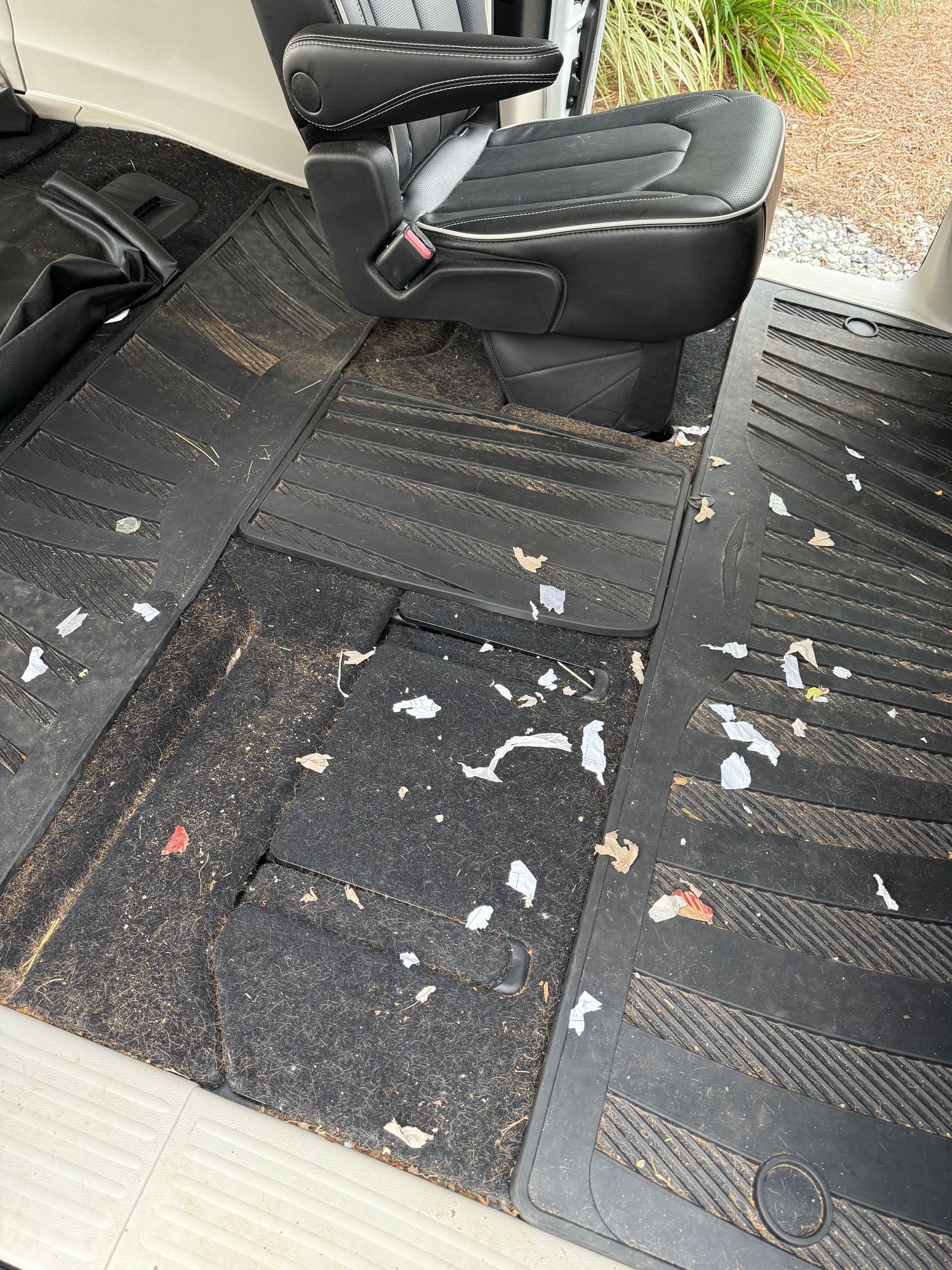 Interior of a vehicle floor, covered in debris and pieces of paper, near a black seat.