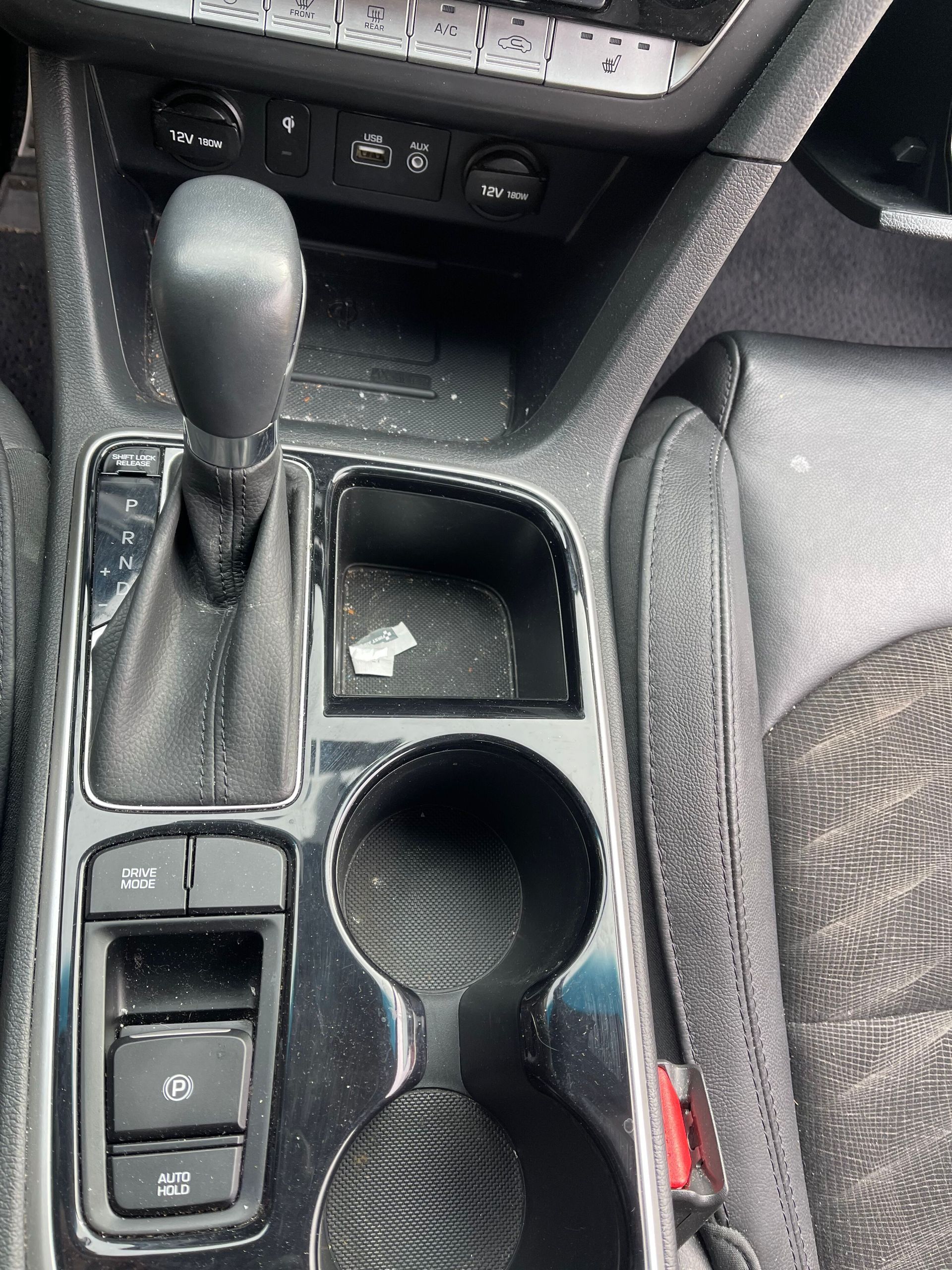 Car's center console with gear shift, cup holder, storage bin, and control buttons.