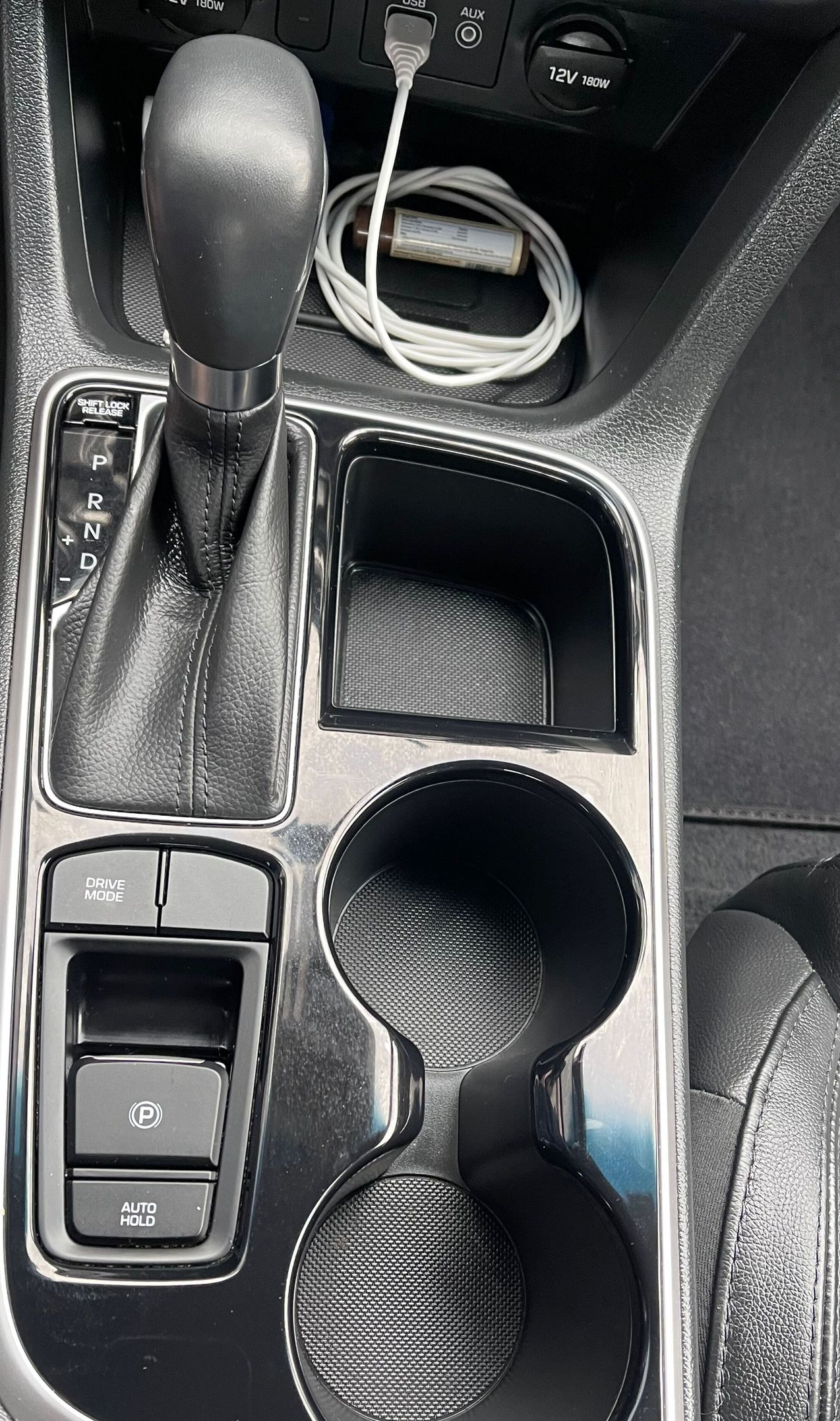 Car console: gearshift, cup holder, storage area, USB cable, buttons.
