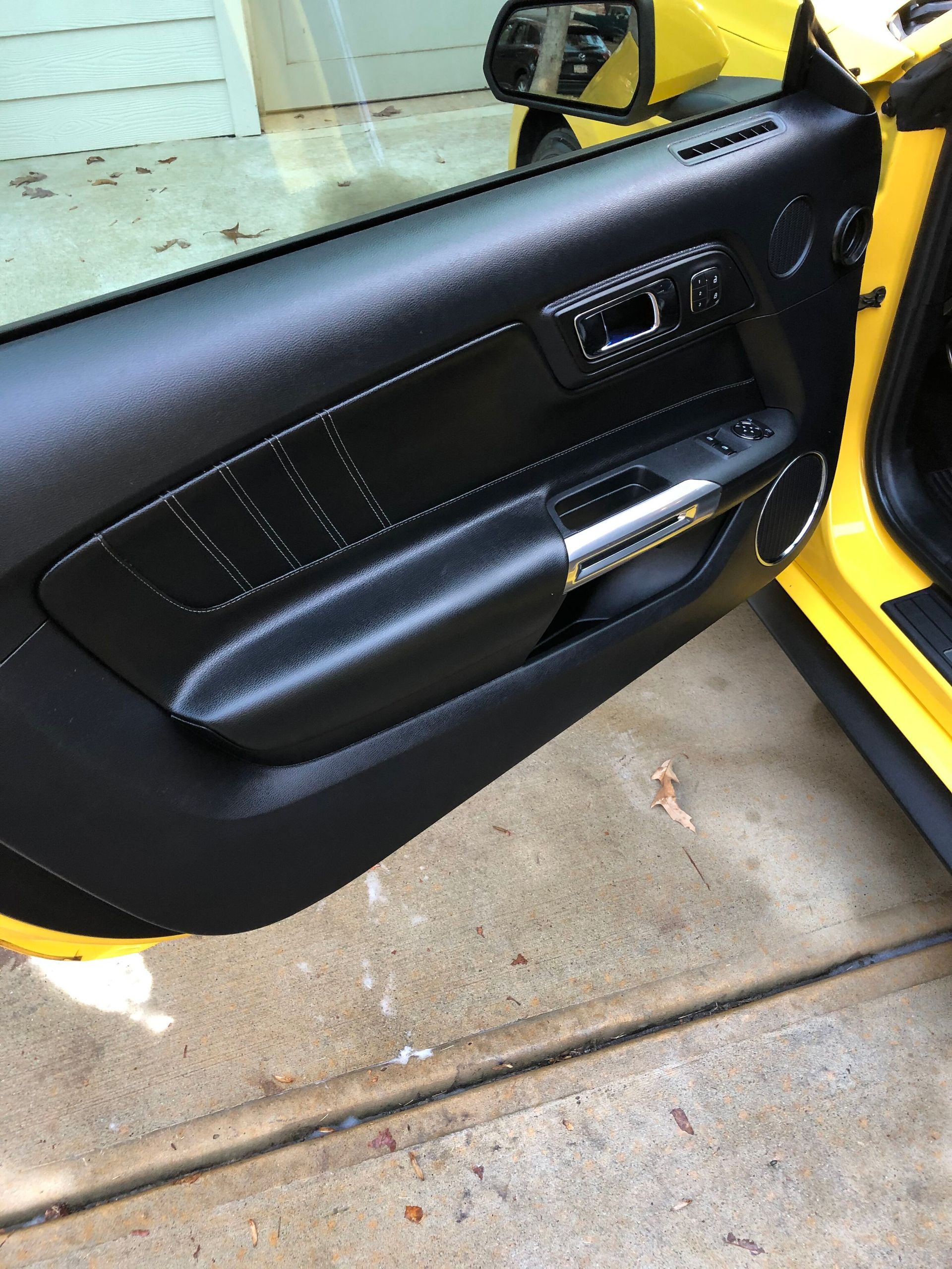 Black interior door panel of a yellow car, featuring a silver handle and power window controls.