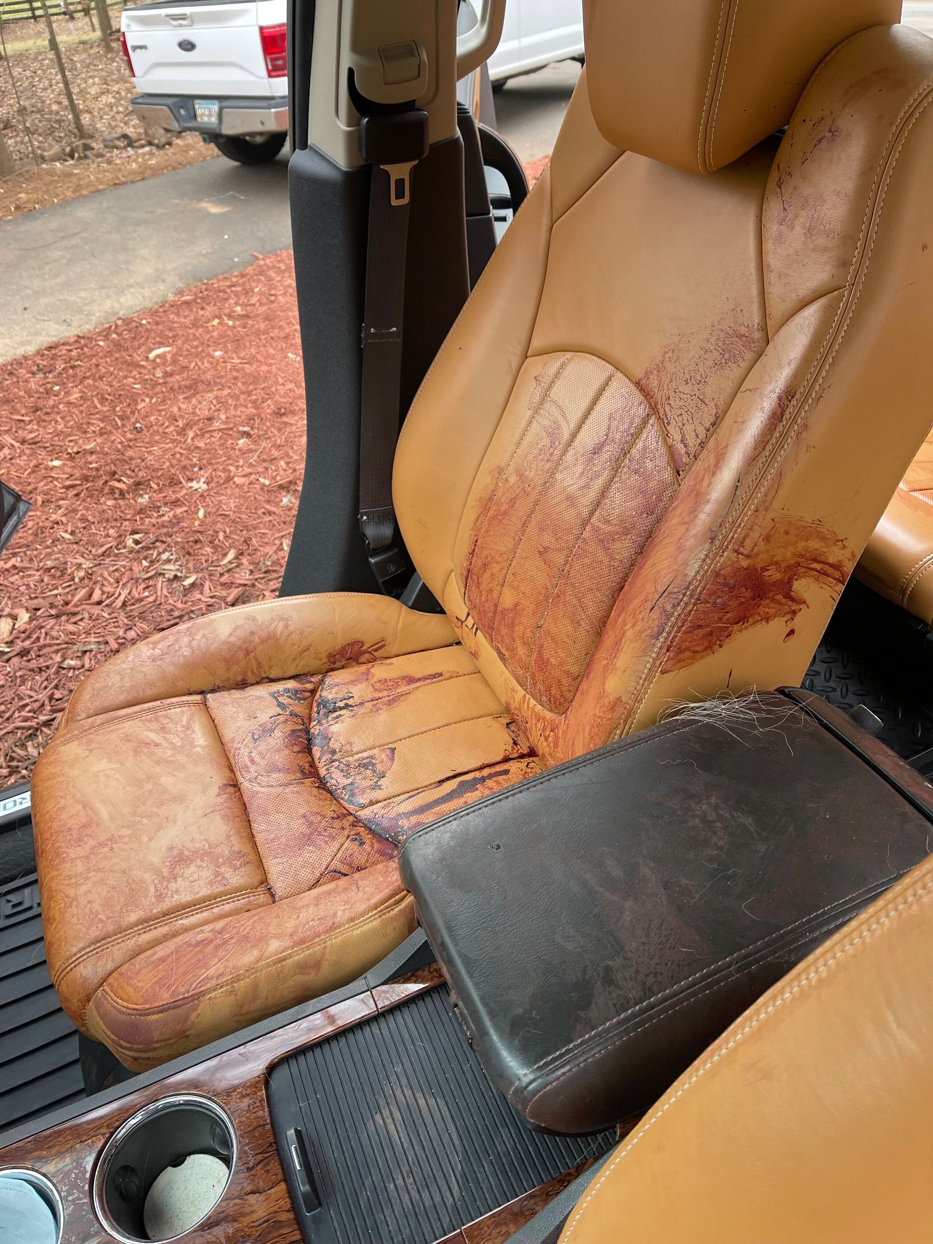 Car interior with severely stained tan leather seats, center console, and cup holders.