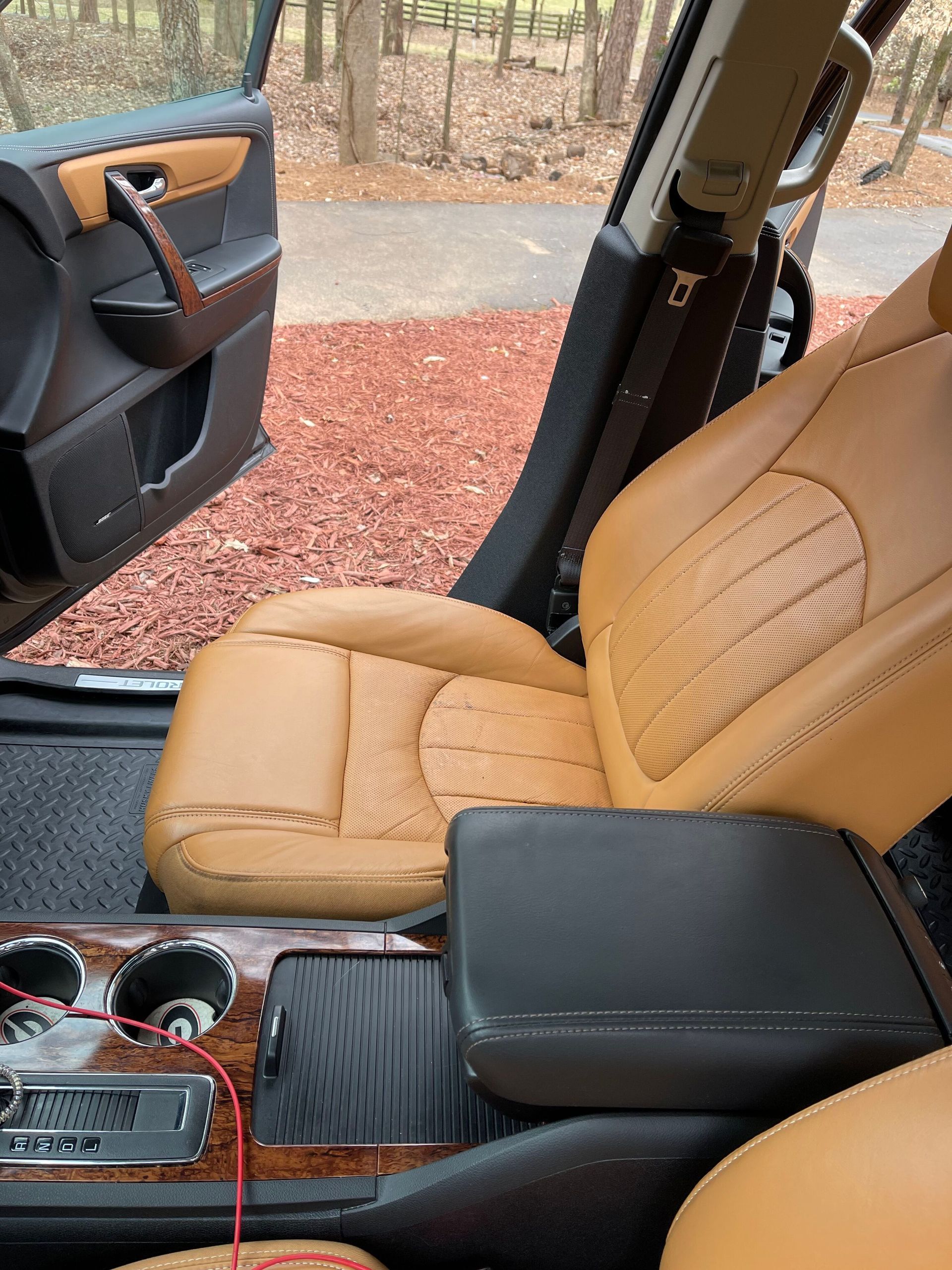 Tan leather car seats with black center console and door. Open car door, outdoor setting.
