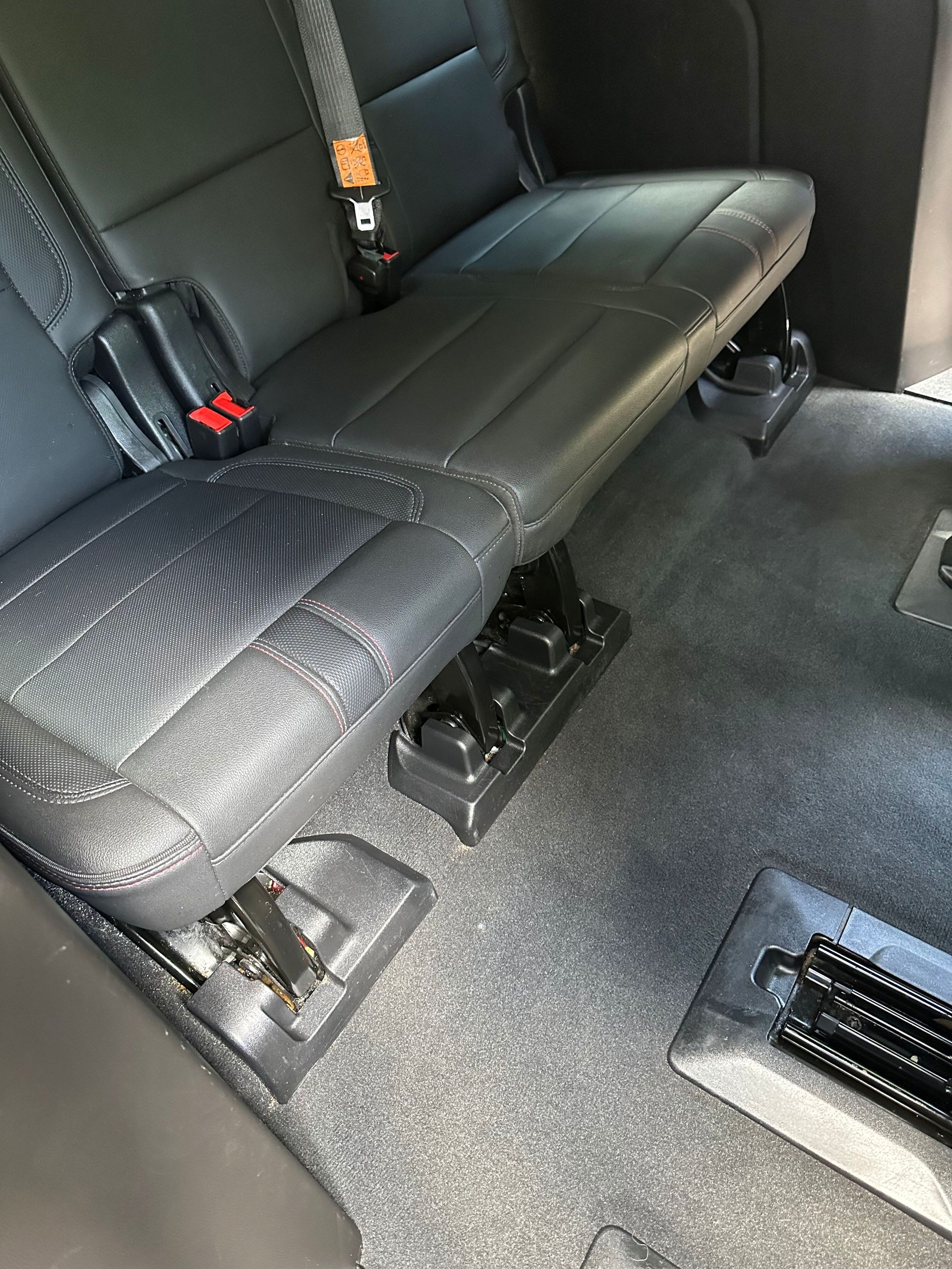 Black car seat folded up in a vehicle. Black carpeted floor.