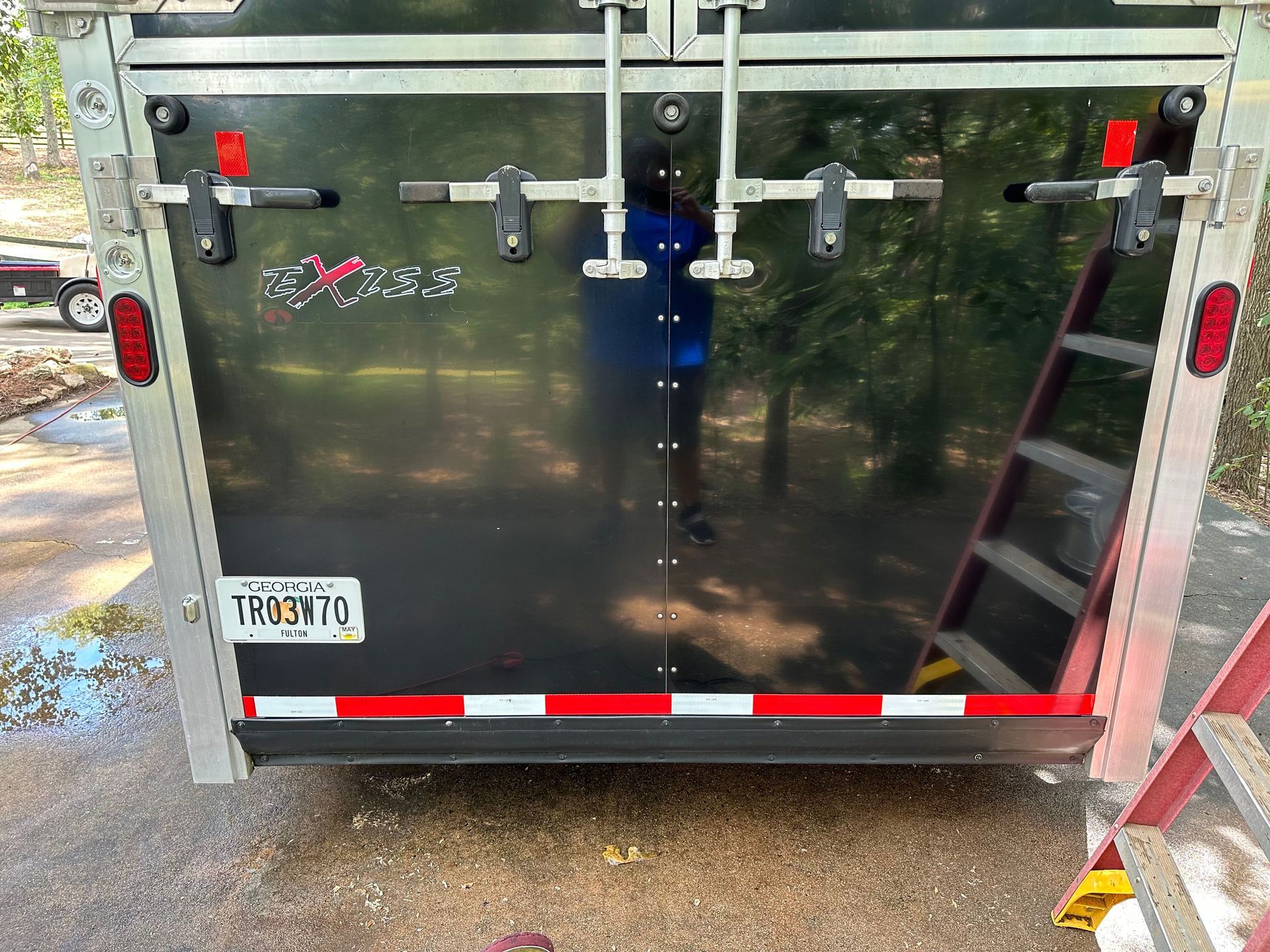 Black horse trailer rear with latches, red reflectors, and license plate. Ladder on the right.