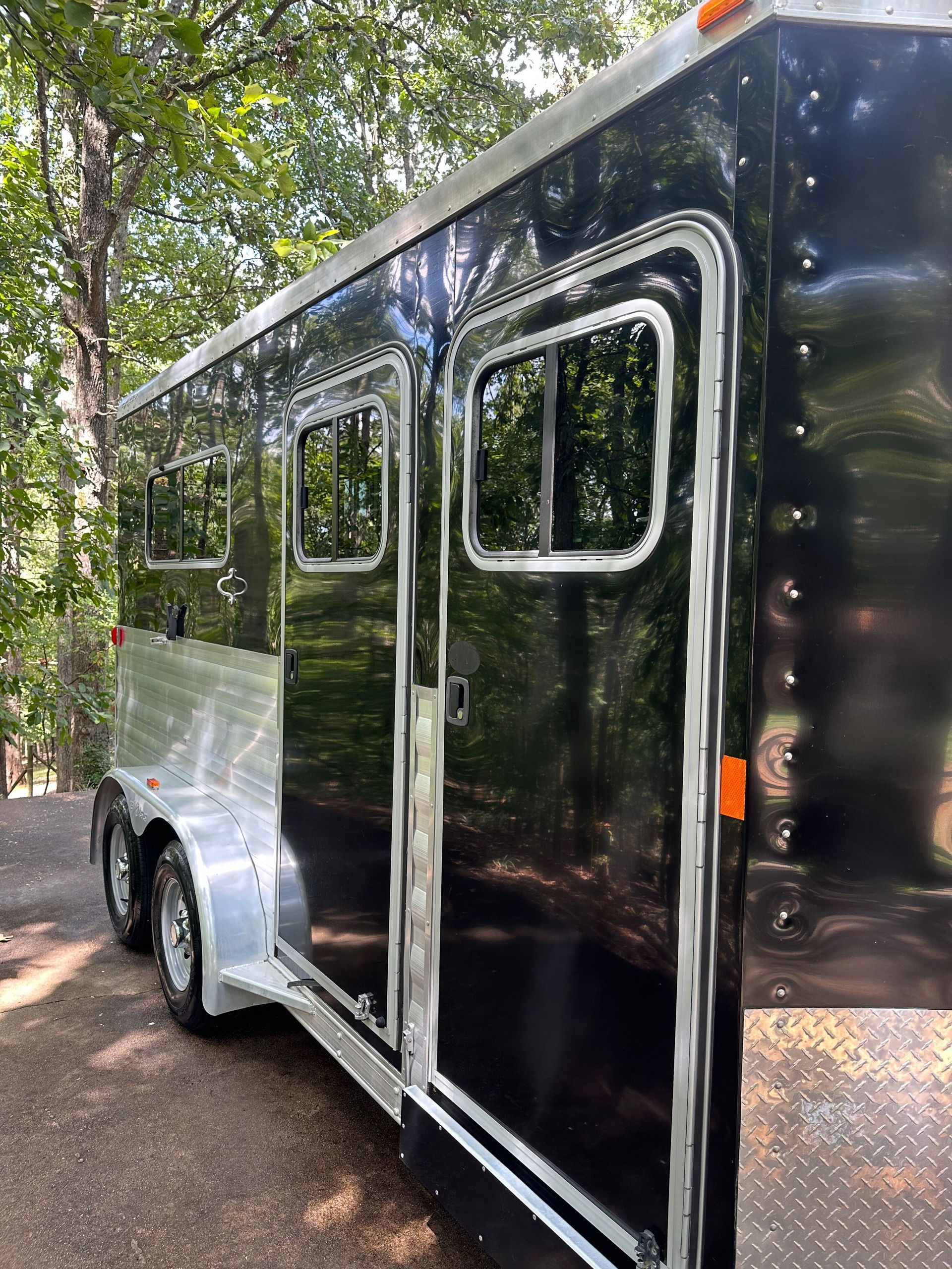 Black and silver horse trailer with windows, parked outdoors.