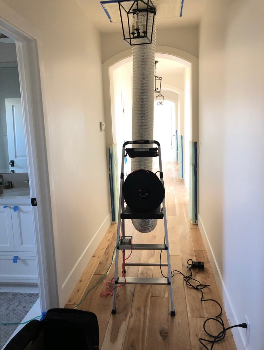 A hallway with a ladder and a fan hanging from the ceiling.
