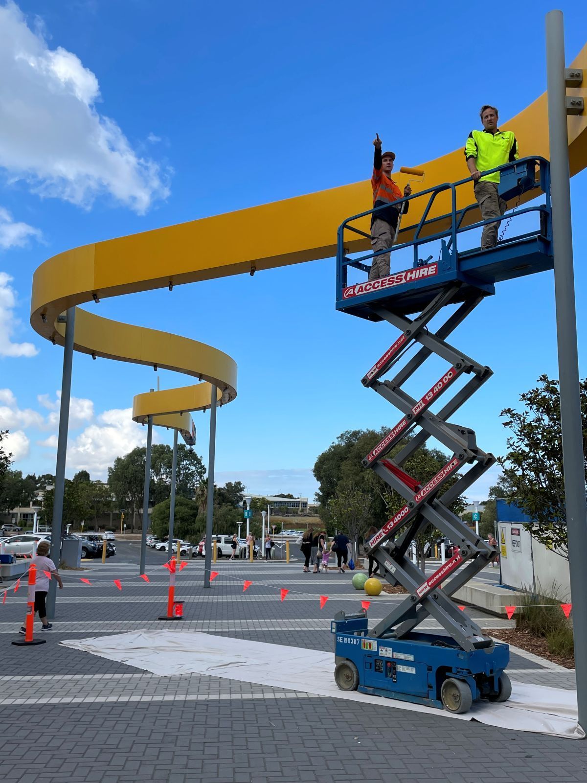 Painters on a lift painting a yellow sculpture.