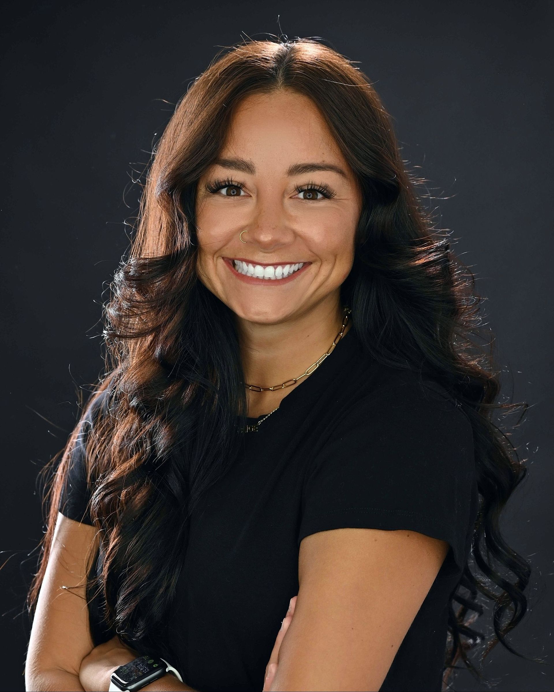 A woman in a black shirt is smiling with her arms crossed.