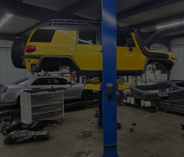 A yellow car is sitting on a lift in a garage | Guaranteed Auto Repair