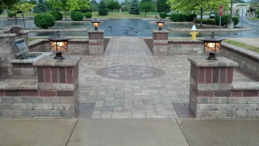 A brick walkway leading to a fountain in a park