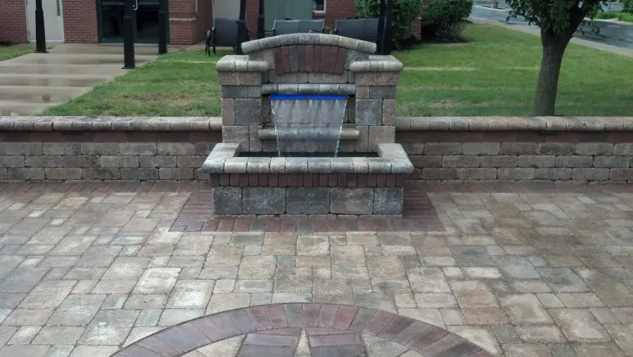 A water fountain is sitting on top of a brick patio.
