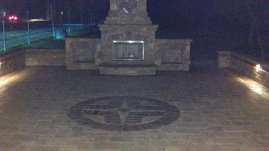 A stone fireplace is lit up at night in a patio area.