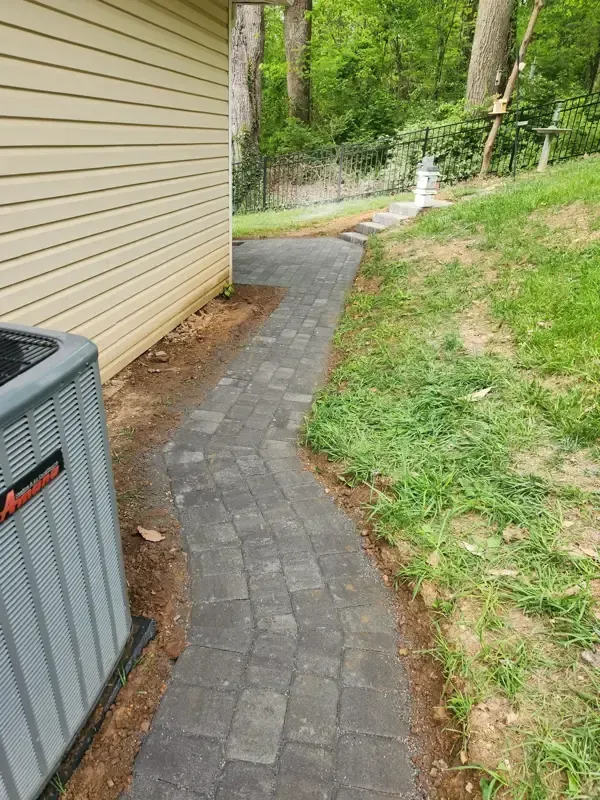 A walkway leading to a house with a gray air conditioner next to it.