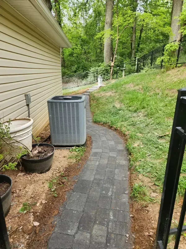 A walkway leading to a house with an air conditioner on the side of it.