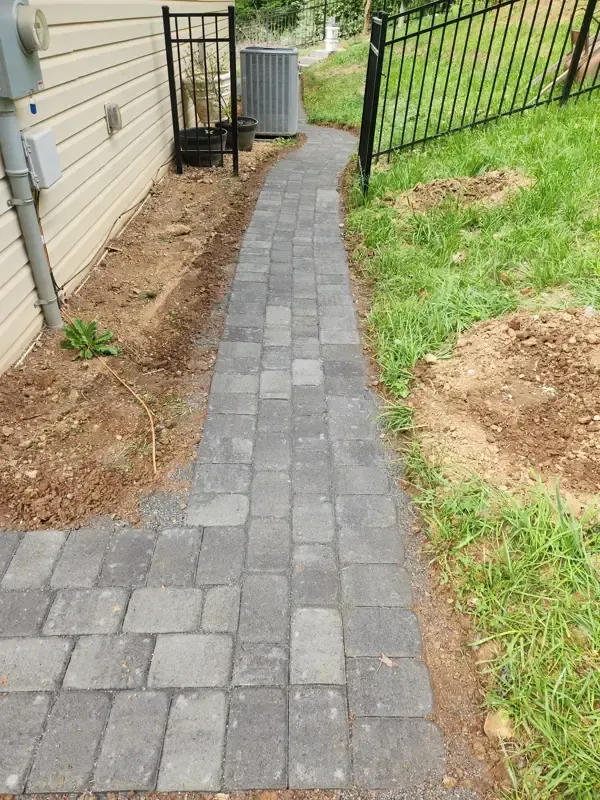A brick walkway leading to a house with a fence in the background.