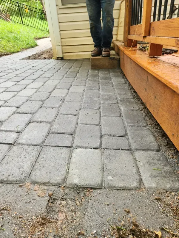 A person is standing on a brick walkway next to a wooden deck.