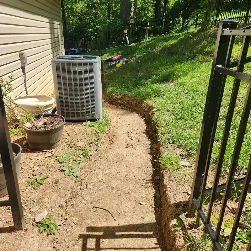 An air conditioner is sitting on the side of a house next to a fence.