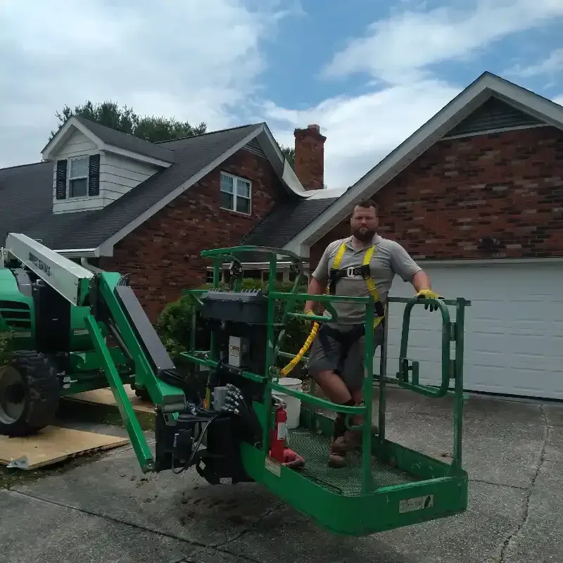 A man is standing in a green lift with a brick house in the background