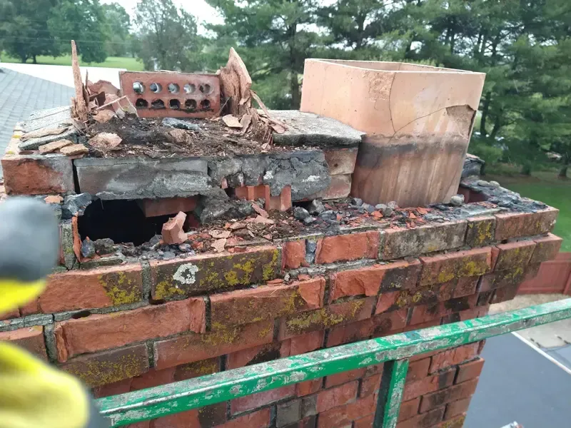 A person is working on a brick chimney with a hammer.