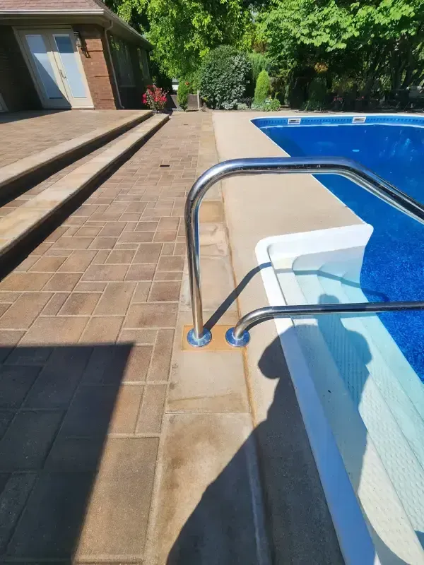 A swimming pool with stairs leading to it and a house in the background.