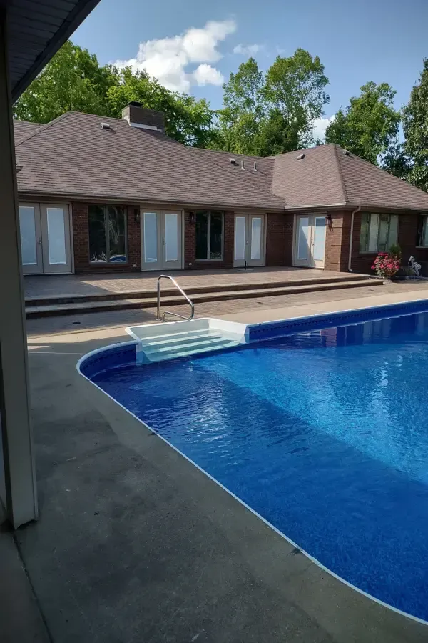 A large swimming pool is in the backyard of a house.