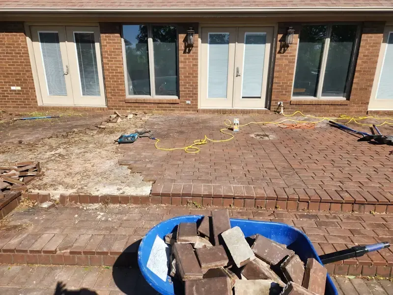 A blue wheelbarrow filled with bricks is sitting in front of a brick house.