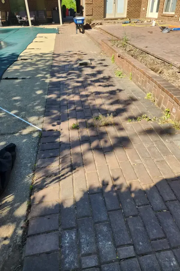 A brick walkway leading to a pool next to a house.