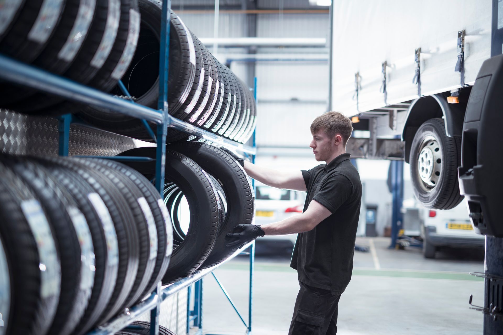 Technician at new tire shop organizing black tires on shelf in modern auto service garage.