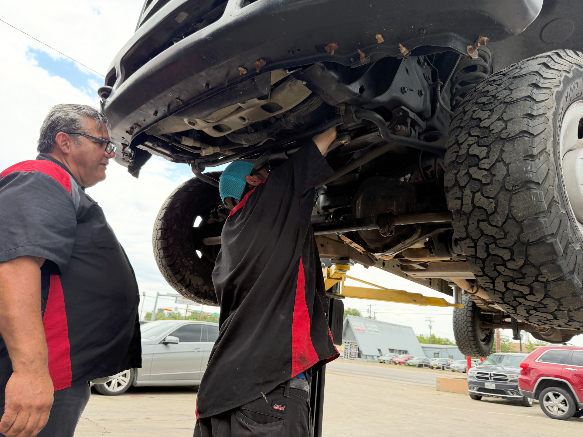 Two mechanics examine the underside of a truck lifted at a repair shop. | Auto Masters Repair Shop