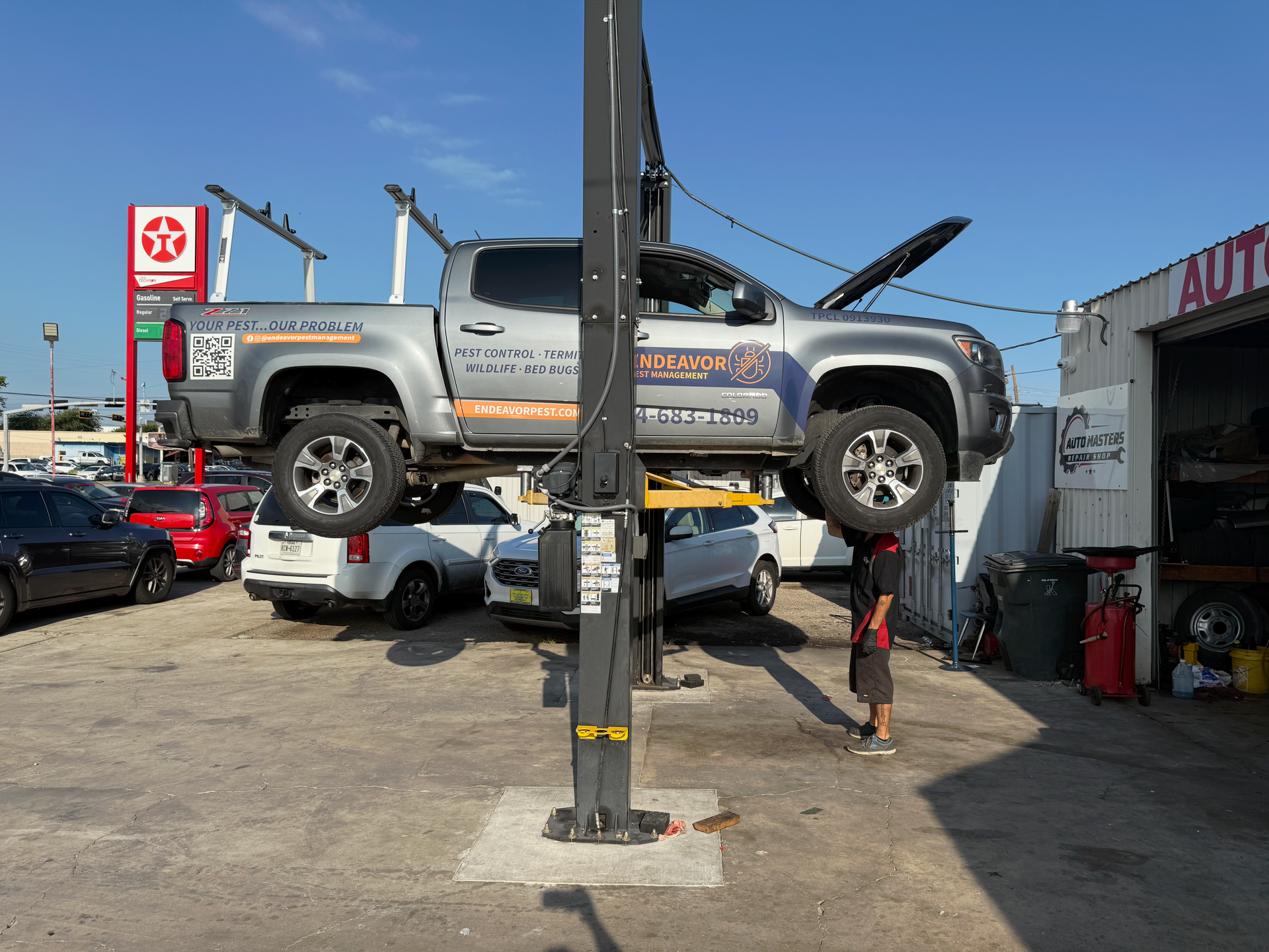 A truck on a lift with hood open at an auto repair shop under a blue sky. | Auto Masters Repair Shop