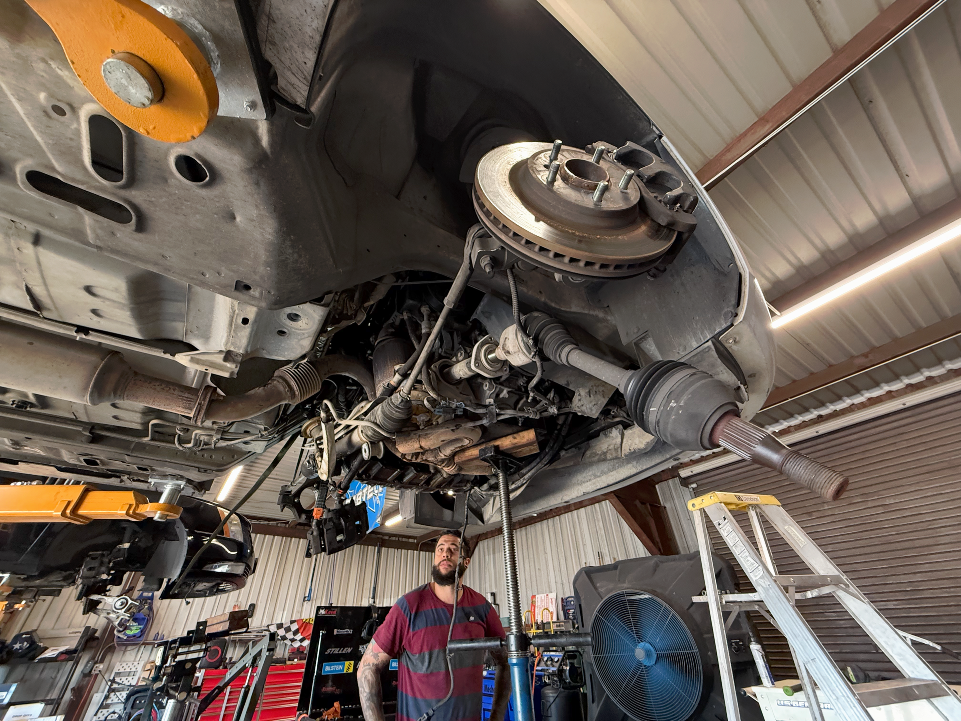 Mechanic under a vehicle, working in a garage. Vehicle suspended with brakes visible. | Auto Masters Repair Shop