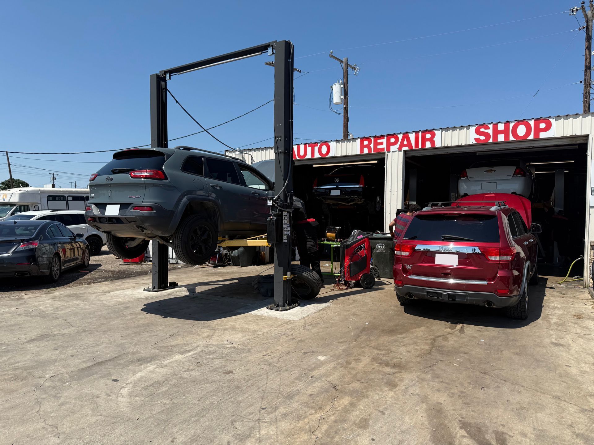 Auto repair shop: Gray Jeep on lift, red SUV in bay, sunny day. | Auto Masters Repair Shop