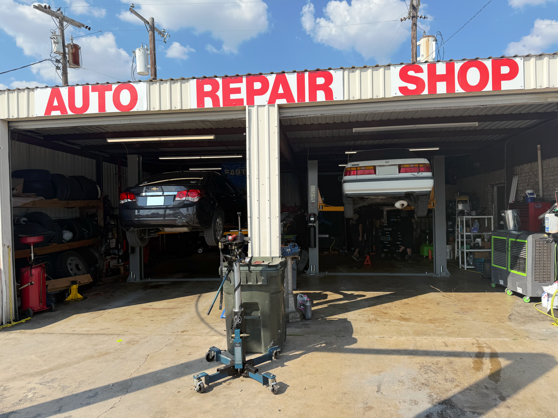 Auto repair shop with cars on lifts under a red sign, sunny day. | Auto Masters Repair Shop
