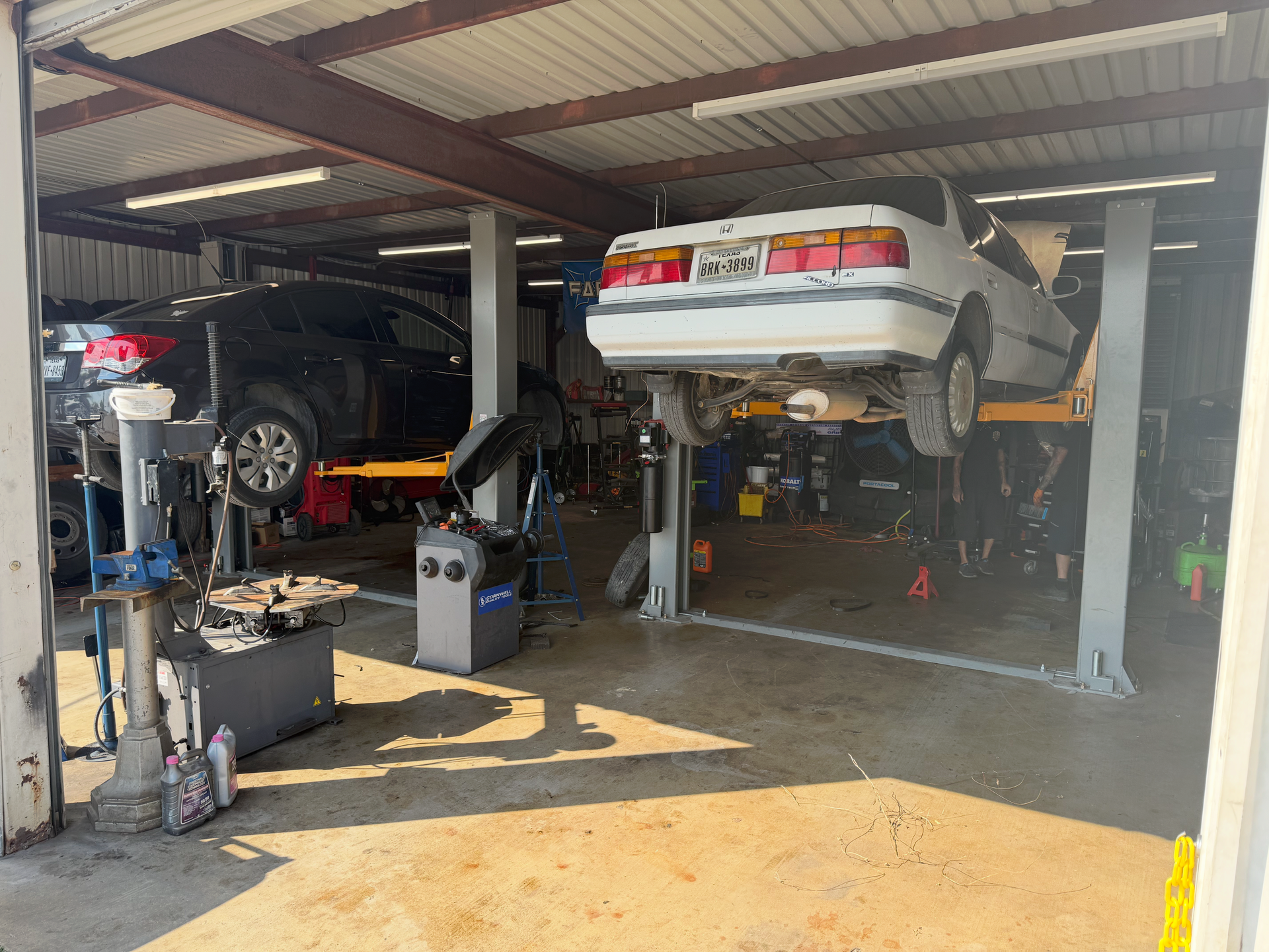 Cars on lifts in a garage; one black, one white.  Tools and equipment visible. | Auto Masters Repair Shop