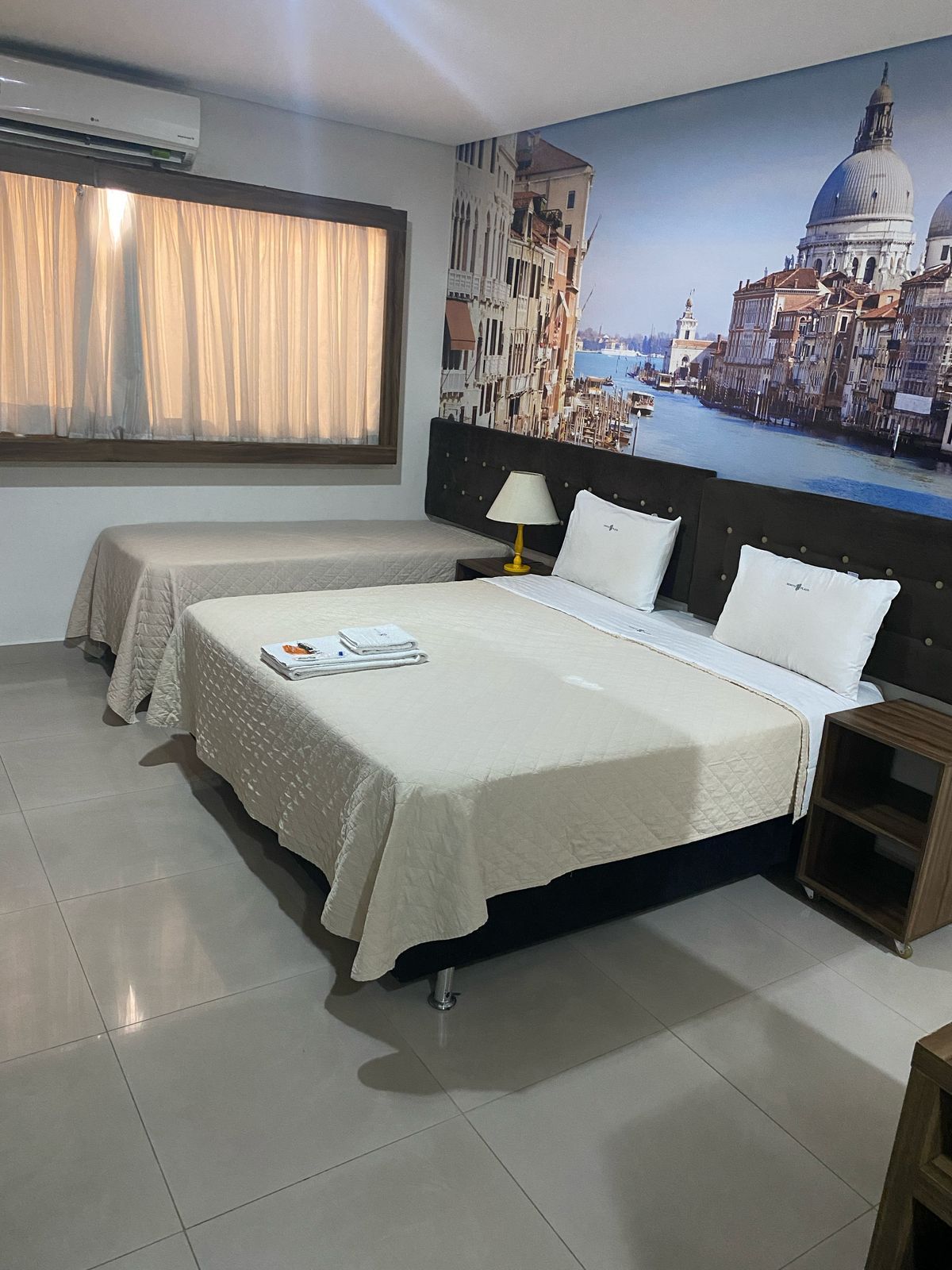 Um quarto de hotel com duas camas e uma foto de Veneza na parede.