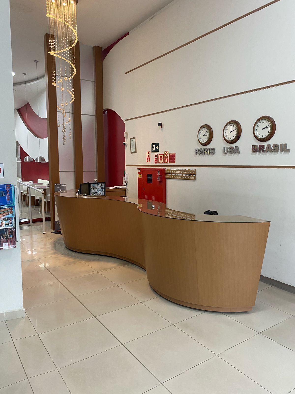 Um lobby de hotel com um balcão de madeira curvo e relógios na parede.