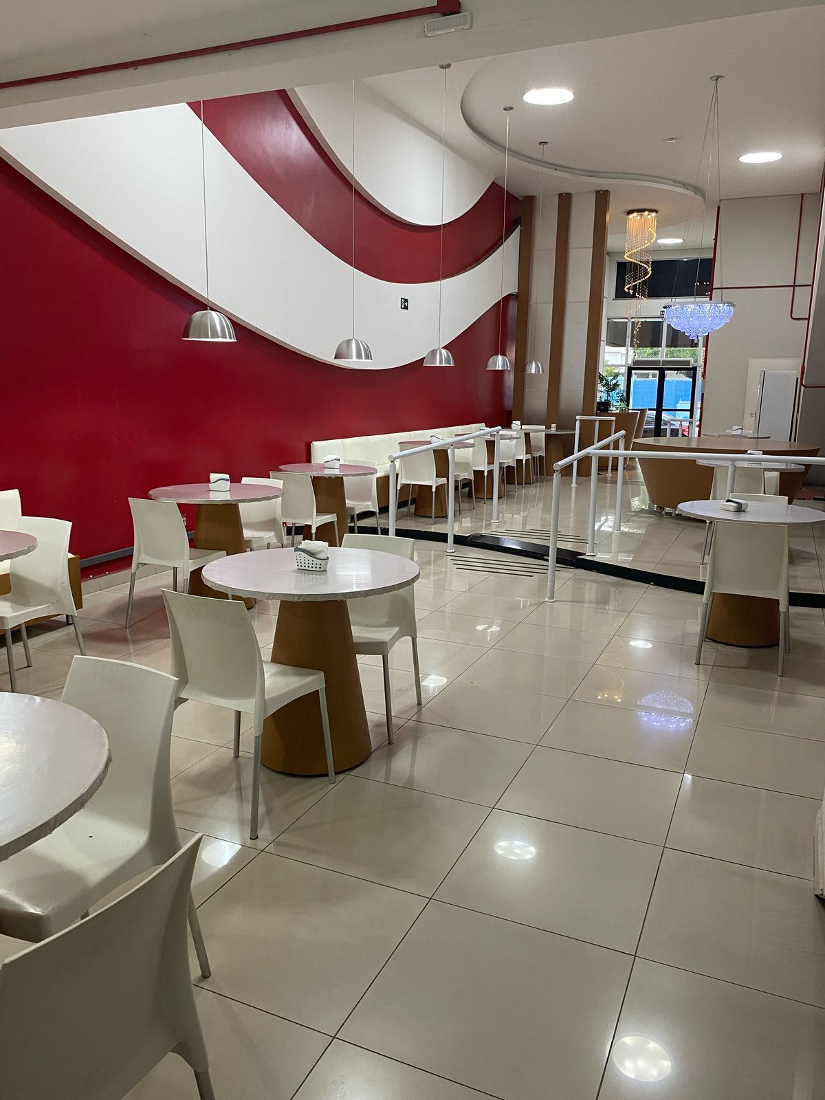 Um restaurante com mesas e cadeiras e uma parede vermelha.