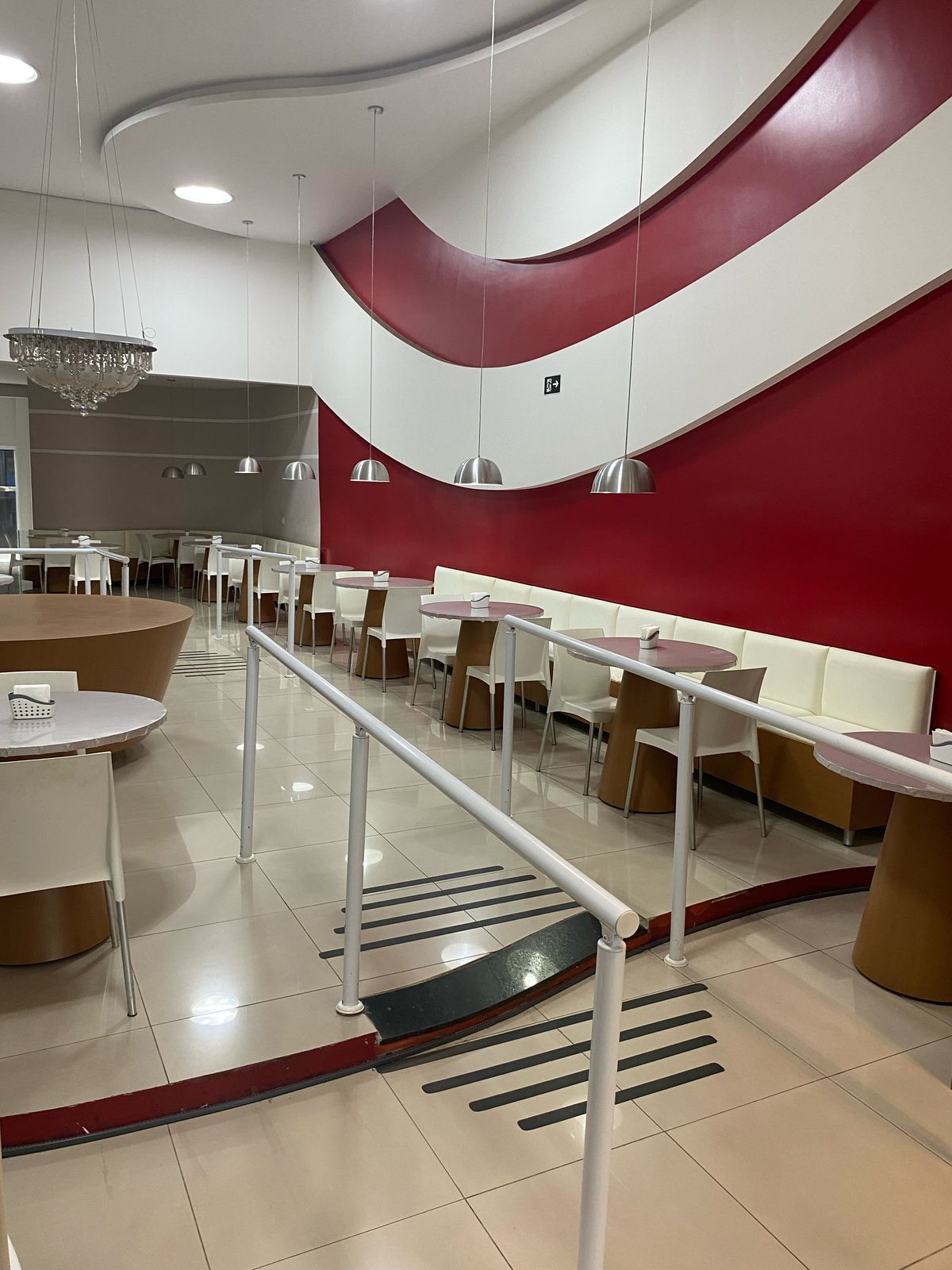 Um restaurante com mesas e cadeiras e uma parede vermelha e branca.