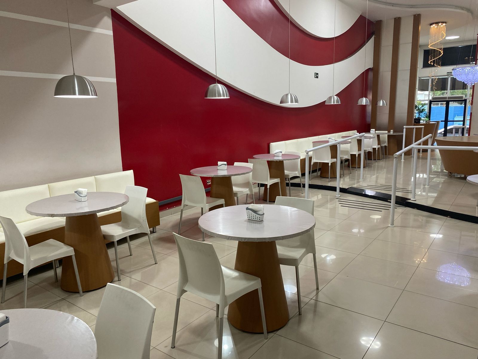 Um restaurante com mesas e cadeiras e uma parede vermelha.