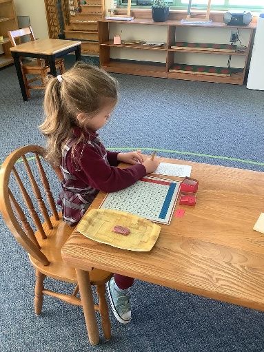 Child seated at a wooden table, working with educational materials in a classroom.
