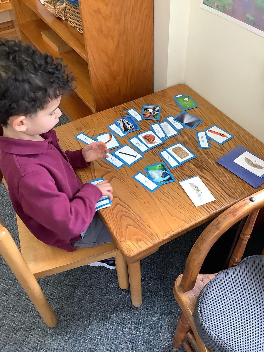 Child seated at a table working on a card matching game with blue cards; wooden furniture.