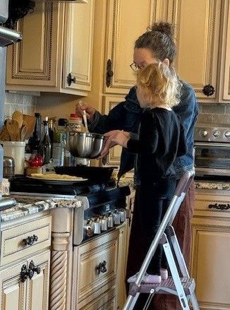 Woman cooking with a child on a step stool in a kitchen.